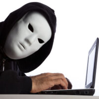 Man in a mask hacking a laptop